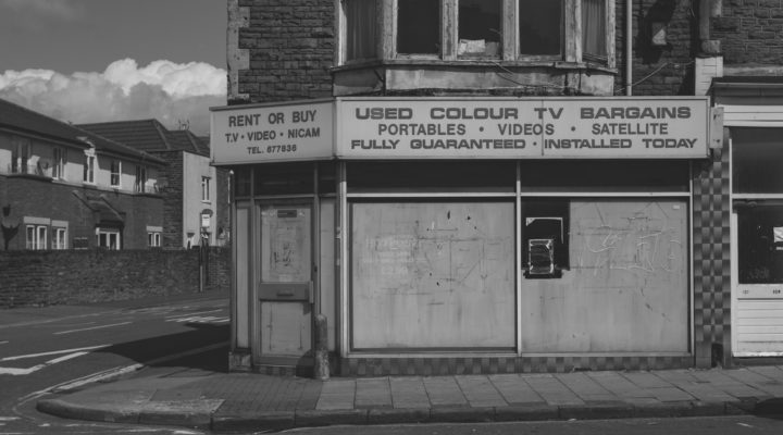 Black and white photo of a closed-down corner shop advertising used TVs.