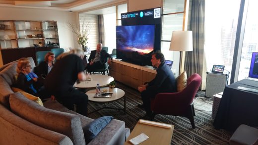 People sitting around a large, high-quality video display in a classy hotel suite.