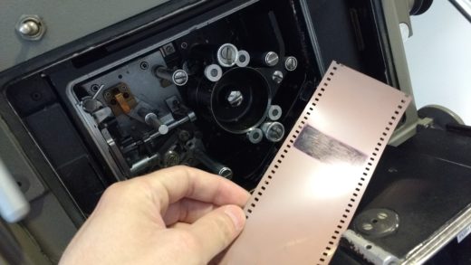 The open mechanism of an Ultra Panavision 70 camera, with a hand holding 65mm film.