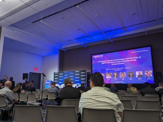 Conference room with plastic chairs, a projection screen, and a podium, seen from the perspective of an attendee.