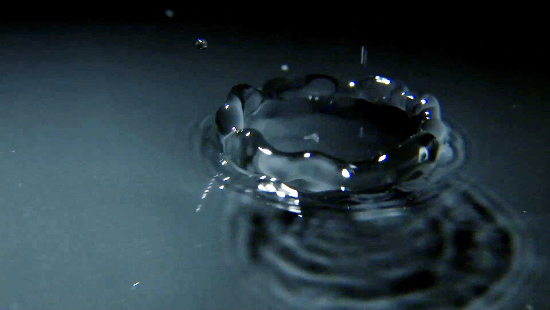 Macro photograph of a drop of water as it falls into a pool. Steel grey tones suggest a modernistic or industrial theme.