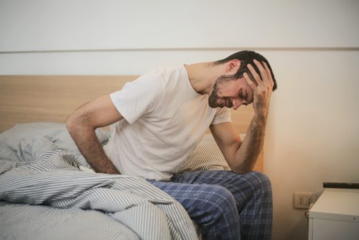 Exhausted man sitting on his bed, holding his head in one hand.