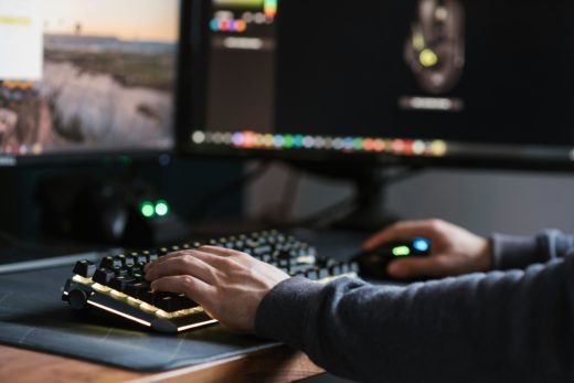 Linux on the desktop? 2 Closeup of a man's hands typing on a black keyboard with monitors indistinctly in the background.