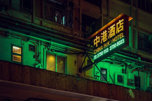 2025 in review: What the people want 4 The outside wall of a hotel in Hong Kong, made grungy with peeling paint and strewn with air conditioning plant, illuminated in saturated green and yellow with an illuminated sign in the same shades.