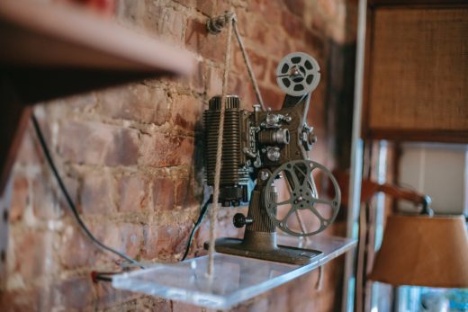 8mm film projector on a glass shelf against a bare brick wall.