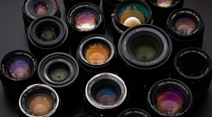 A selection of 1980s-vintage stills photography lenses, moodily-lit on a dark background.