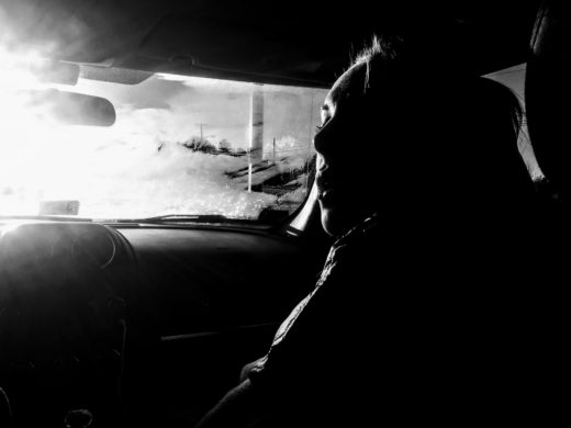 Black and white image of a woman in the passenger seat of a car, heavily backlit by the sun.