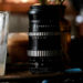 Pentacon lens with zebra-striped barrel on a desk next to a drinking glass.