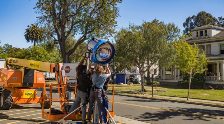 Image of a lighting crew rigging a large HMI on a stand.